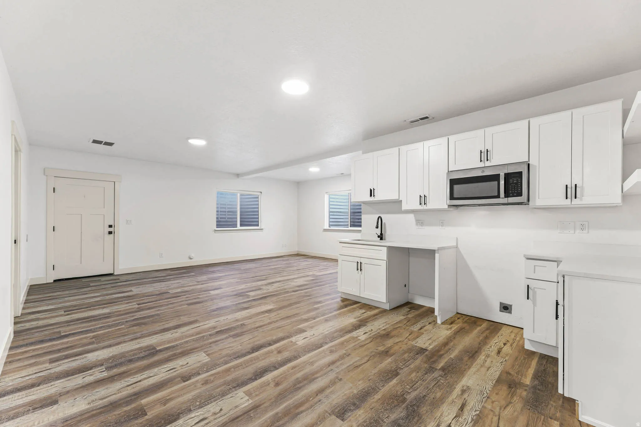 Kitchen featuring white cabinetry, light countertops, dark wood-style flooring, stainless steel microwave, and recessed lighting