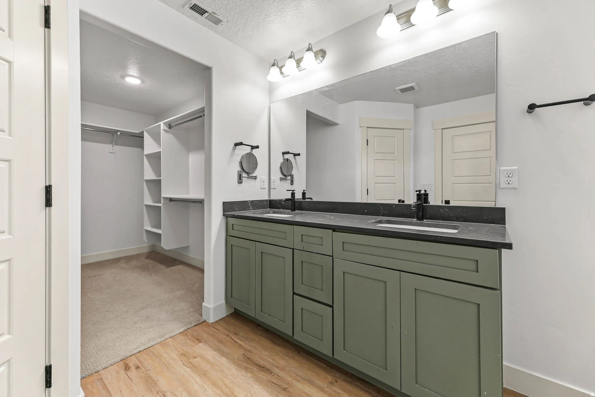 Full bath with a textured ceiling, double vanity, a walk in closet, and light wood-type flooring