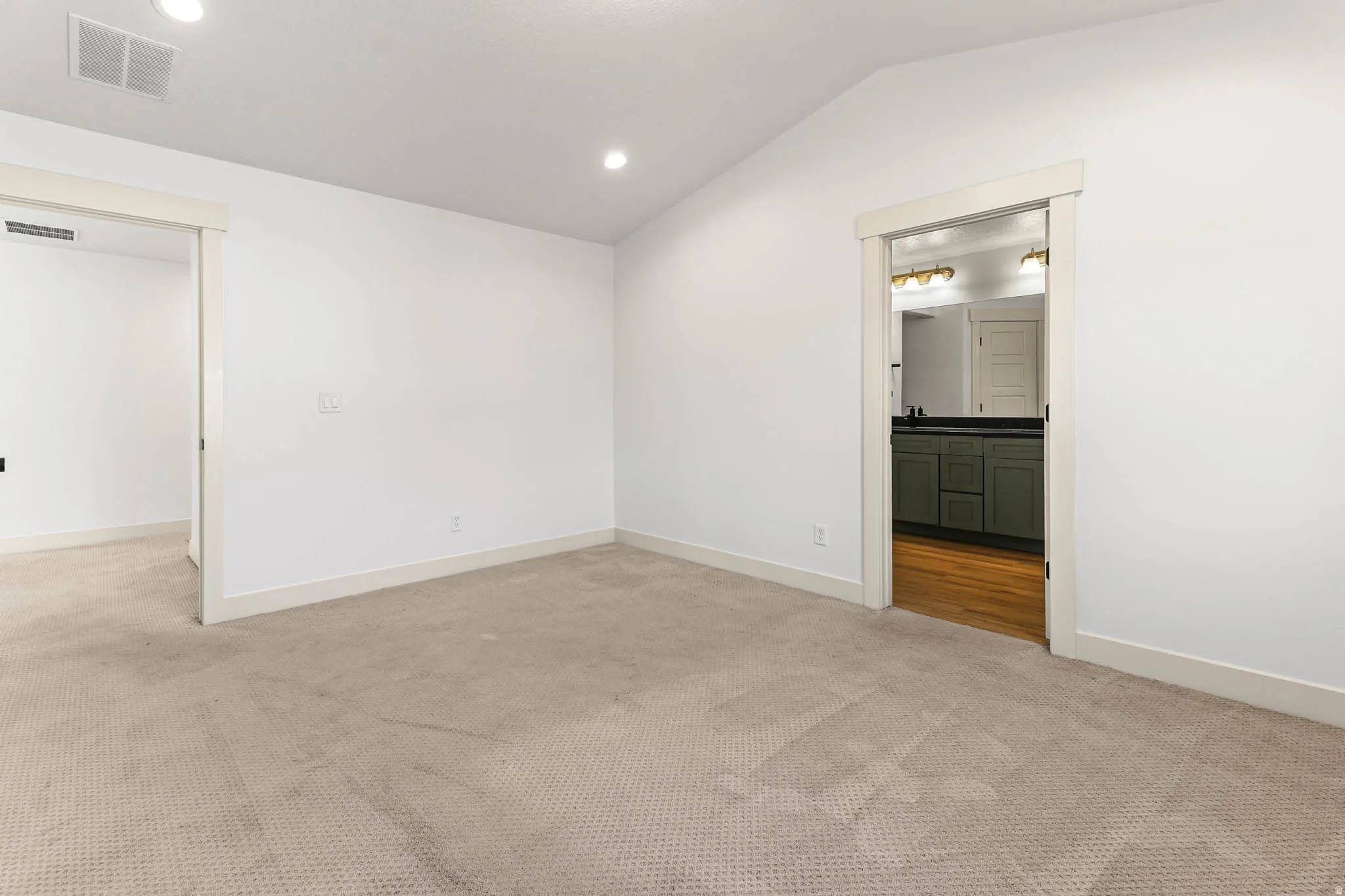Unfurnished bedroom with vaulted ceiling, light carpet, recessed lighting, and connected bathroom