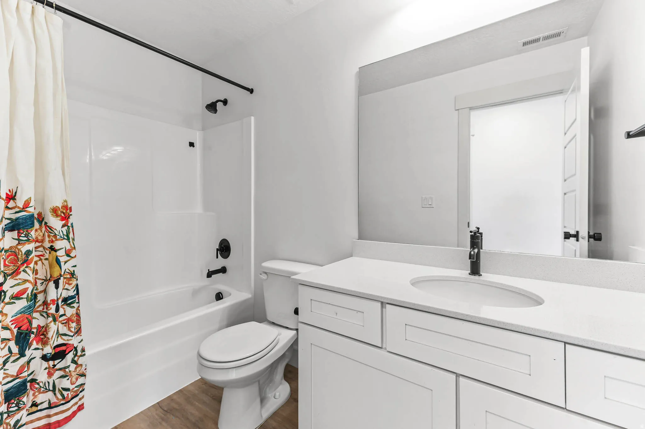 Bathroom featuring vanity, shower / bathtub combination with curtain, and dark wood-type flooring