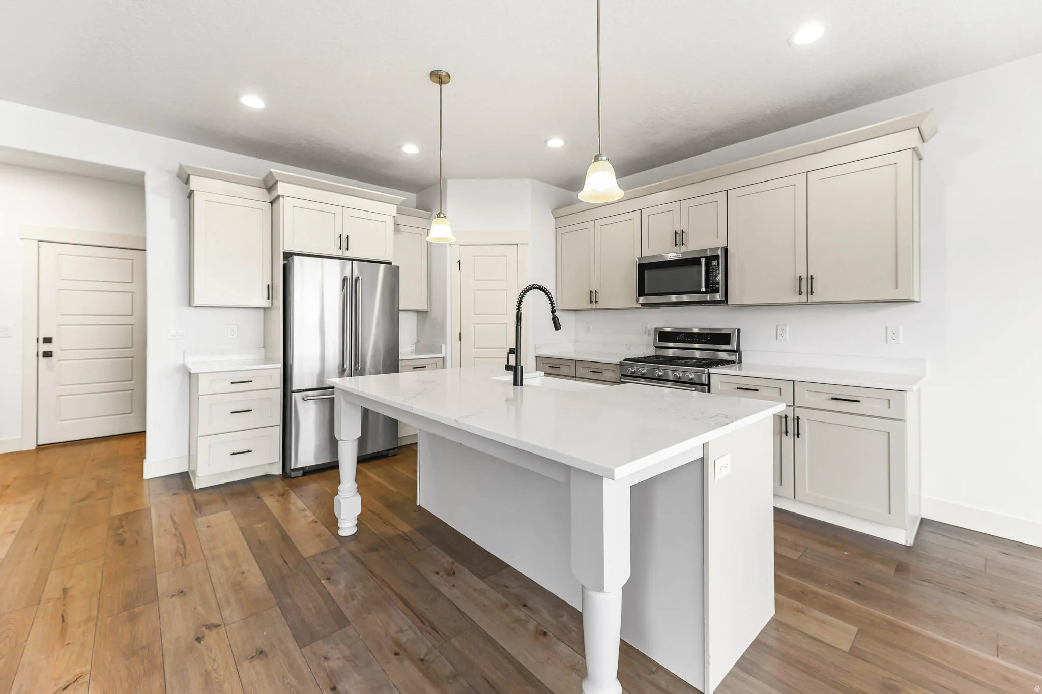 Kitchen featuring stainless steel appliances, pendant lighting, a kitchen island with sink, light stone countertops, and dark wood-style flooring