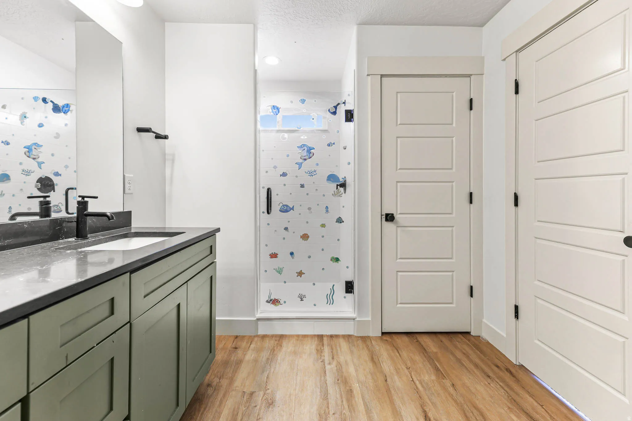 Full bath with a shower stall, vanity, light wood finished floors, and a textured ceiling