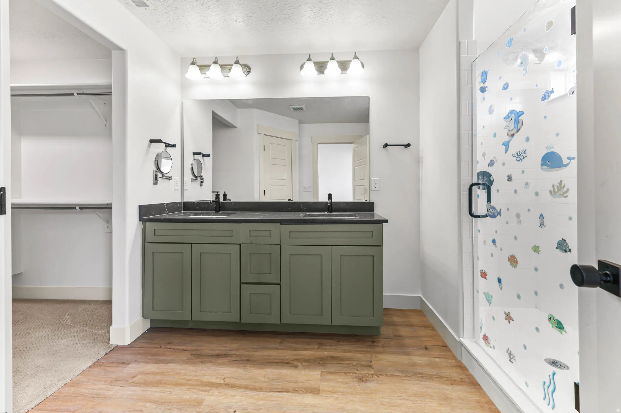 Bathroom with double vanity, a stall shower, light wood finished floors, a walk in closet, and a textured ceiling