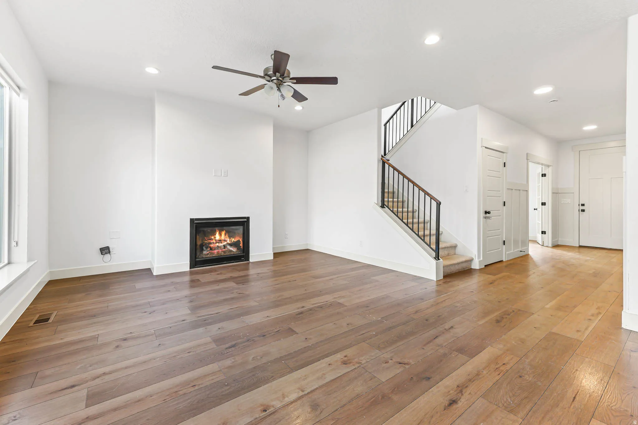Unfurnished living room with stairs, a glass covered fireplace, light wood finished floors, recessed lighting, and ceiling fan