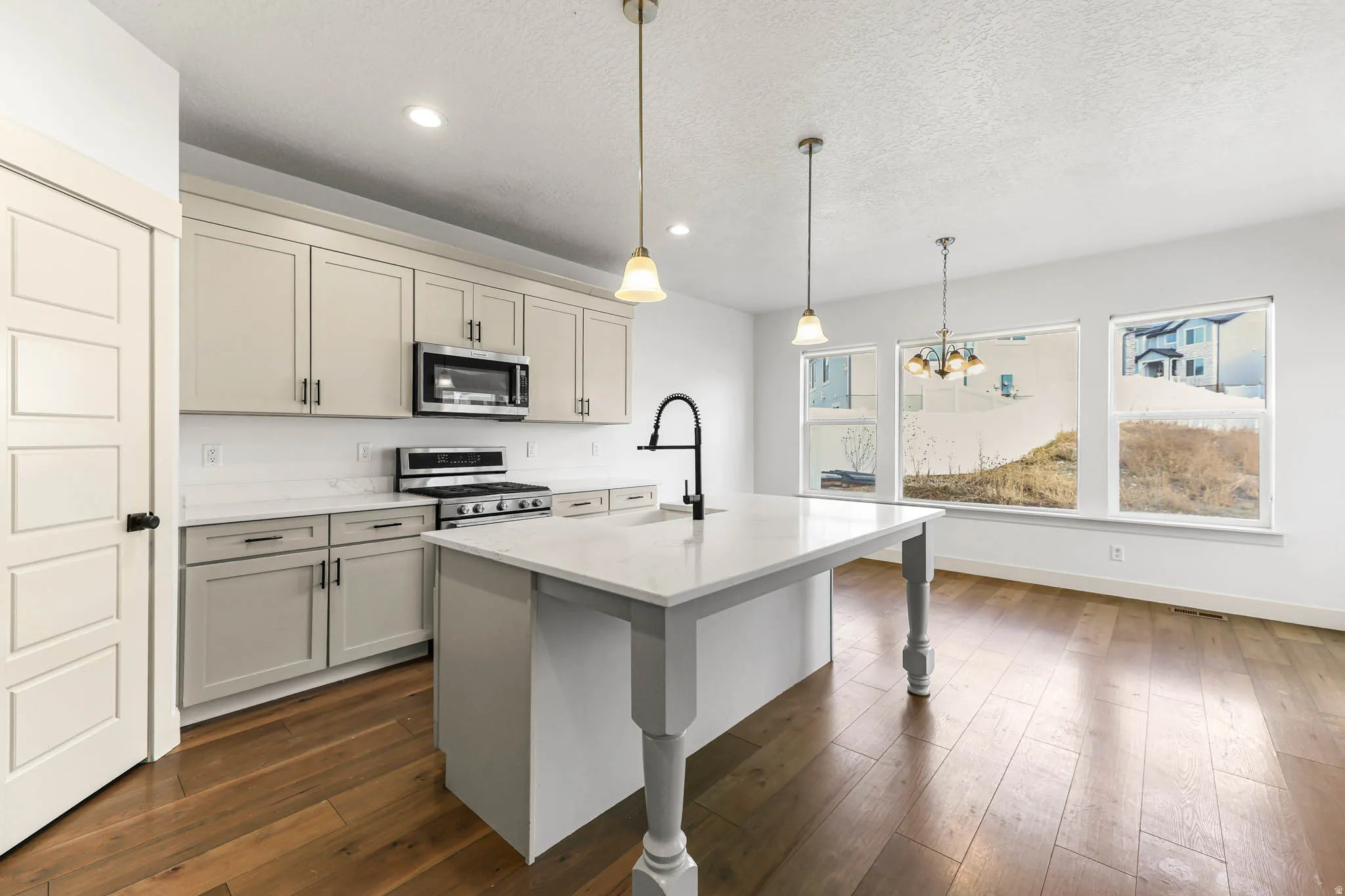 Kitchen with appliances with stainless steel finishes, light stone counters, decorative light fixtures, an island with sink, and dark wood-style flooring