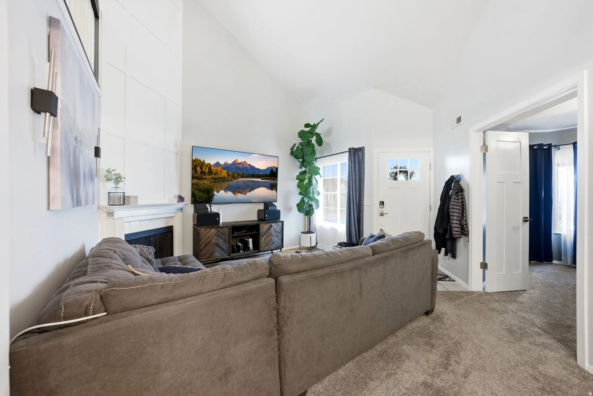 Living room with a fireplace, light colored carpet, and high vaulted ceiling