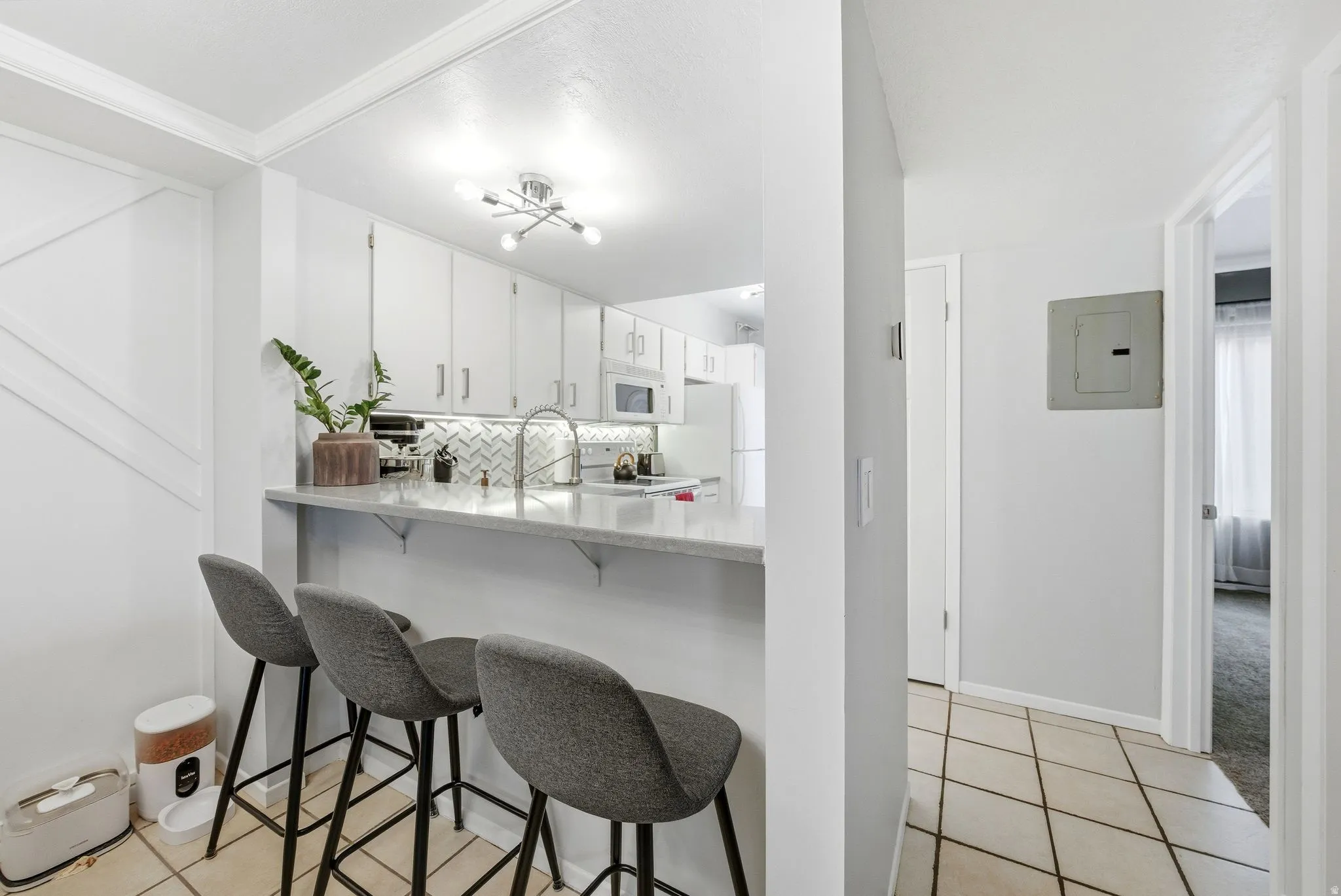 Kitchen with a kitchen bar, electric panel, light tile patterned floors, and white cabinets