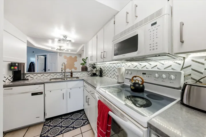 Kitchen featuring white appliances, white cabinets, tasteful backsplash, and light tile patterned floors