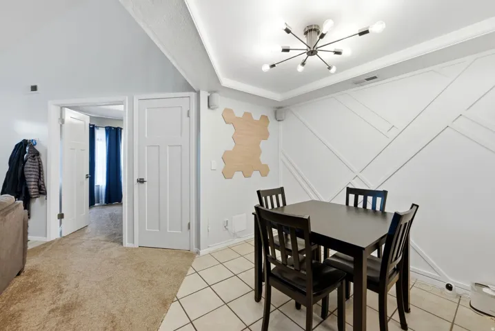 Dining space featuring a chandelier, light colored carpet, a decorative wall, light tile patterned floors, and crown molding