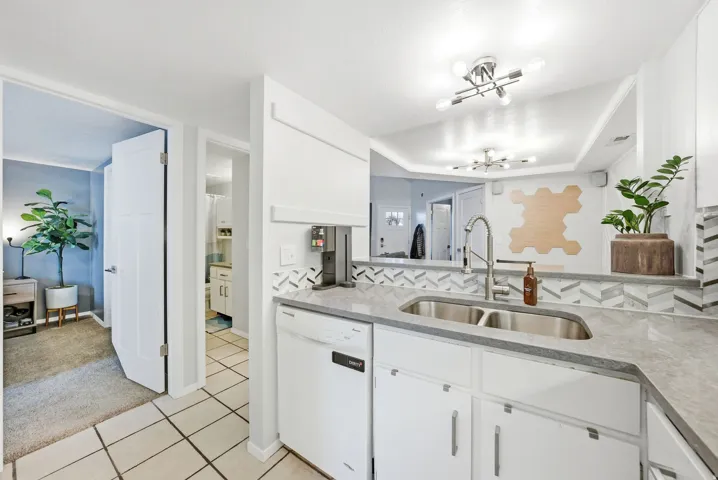 Kitchen with white dishwasher, light stone counters, white cabinets, a tray ceiling, and light carpet
