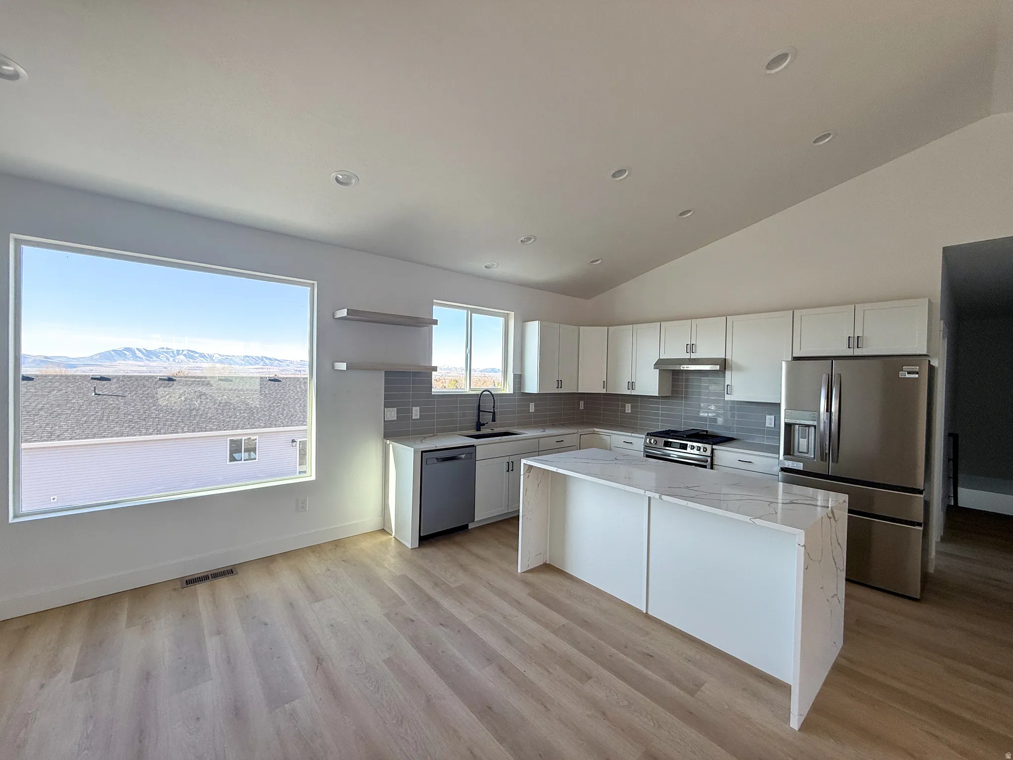Kitchen with light stone countertops, stainless steel appliances, decorative backsplash, white cabinetry, and high vaulted ceiling
