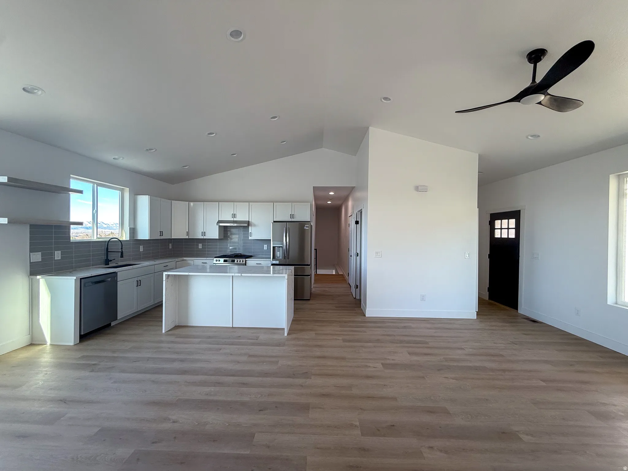 Kitchen featuring open floor plan, white cabinets, a kitchen island, lofted ceiling, and backsplash