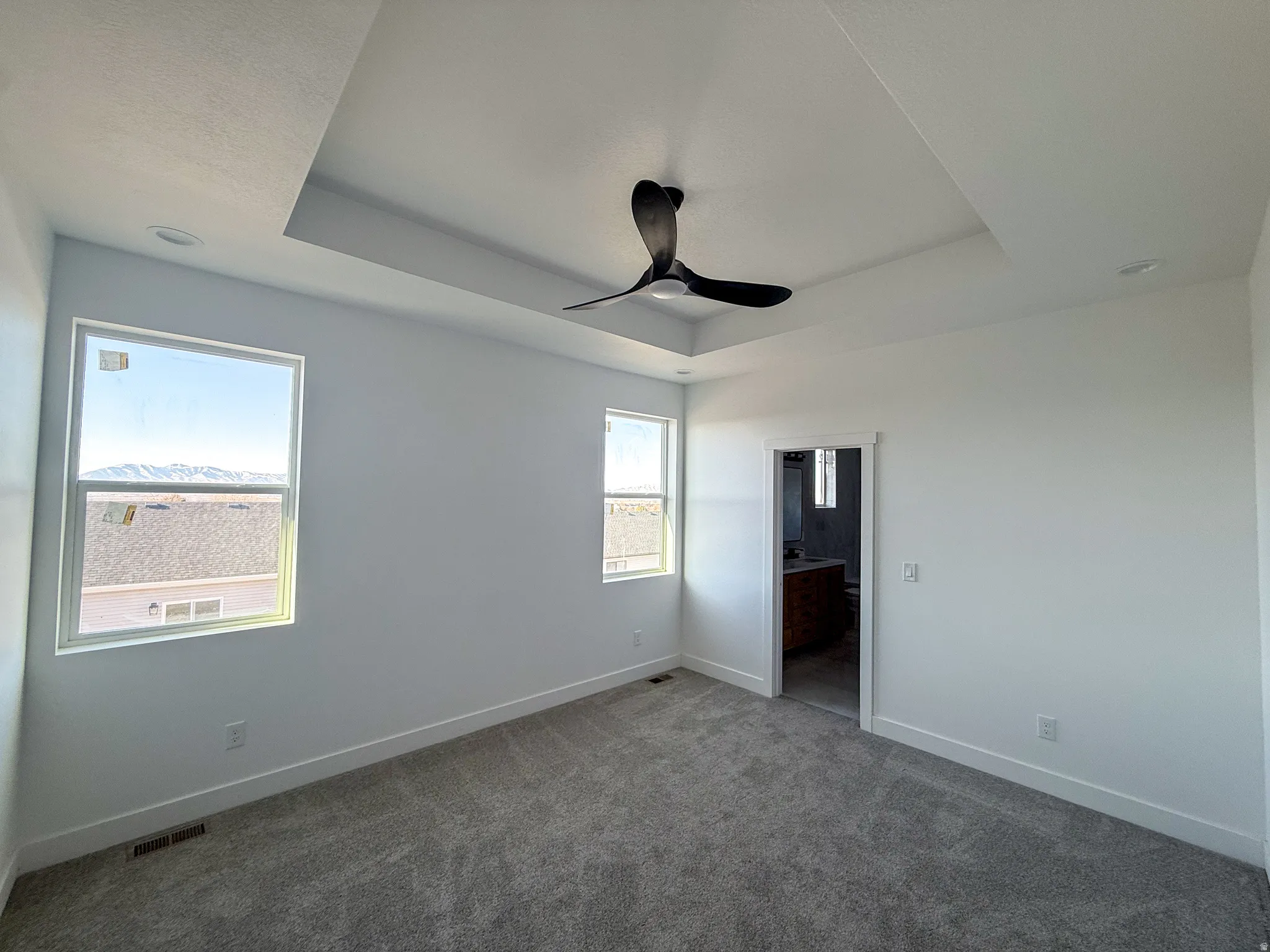 Unfurnished bedroom with a raised ceiling, carpet floors, ceiling fan, and ensuite bathroom