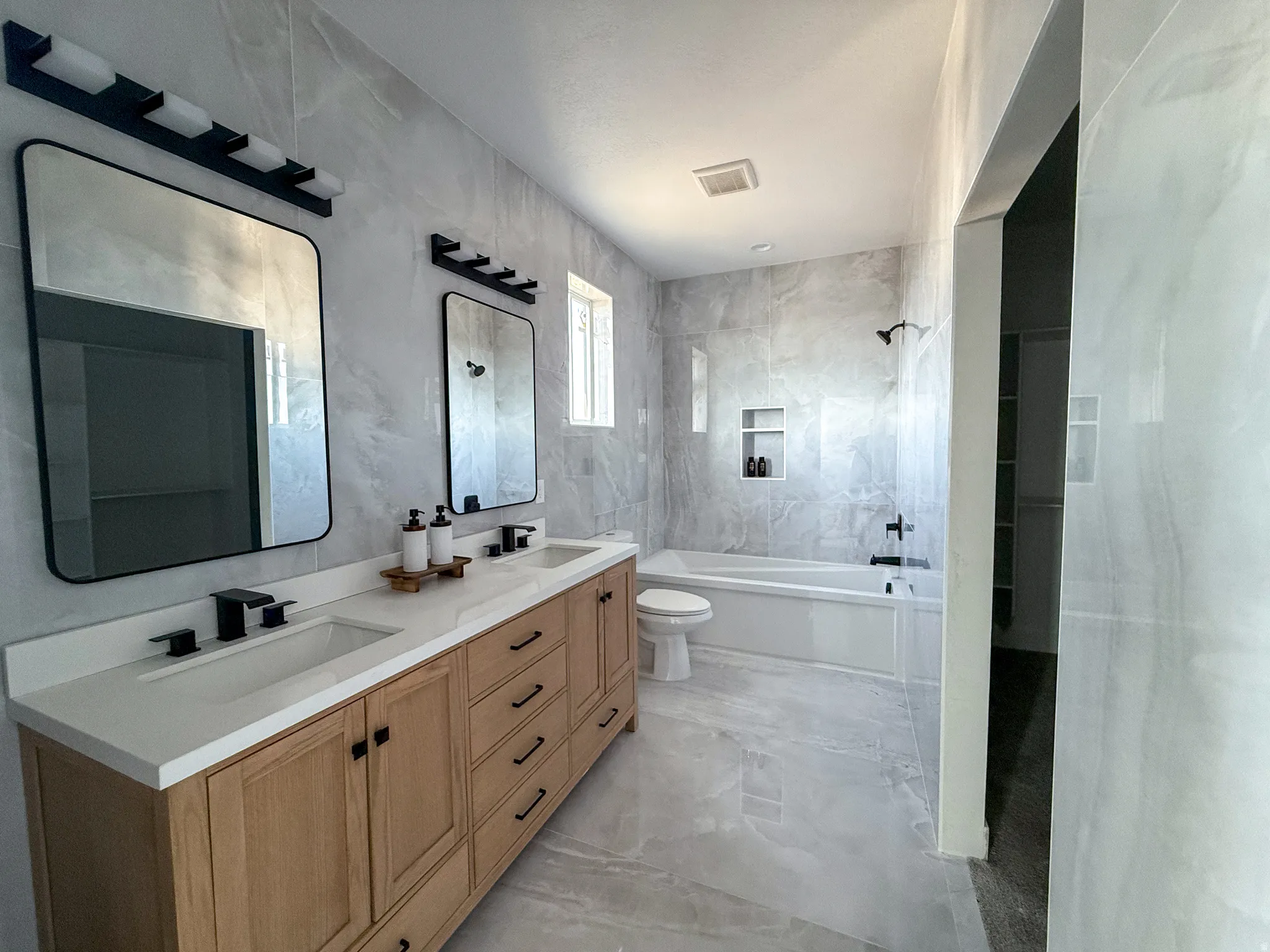 Bathroom featuring double vanity, light marble finish floors, and tile walls