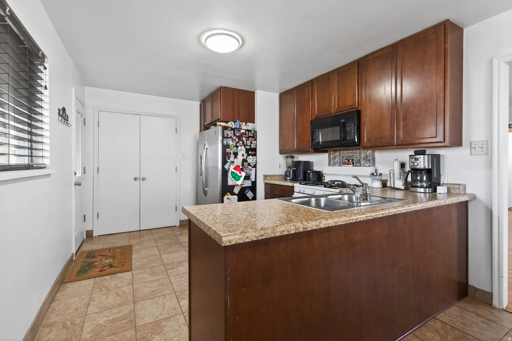 Kitchen featuring a peninsula, light countertops, stainless steel fridge with ice dispenser, black microwave, and light tile patterned floors