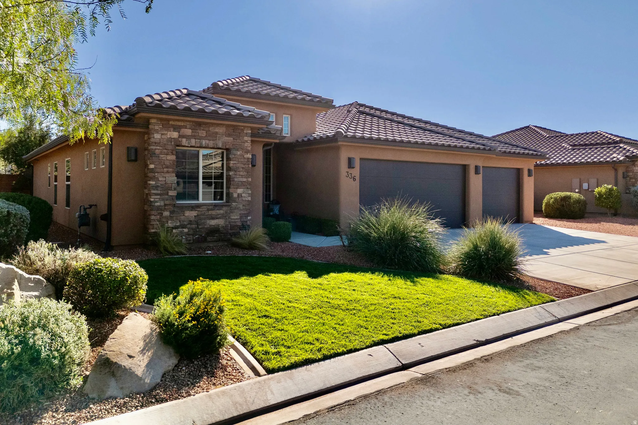 View of front of home featuring a front yard, concrete driveway, stucco siding, stone siding, and an attached garage