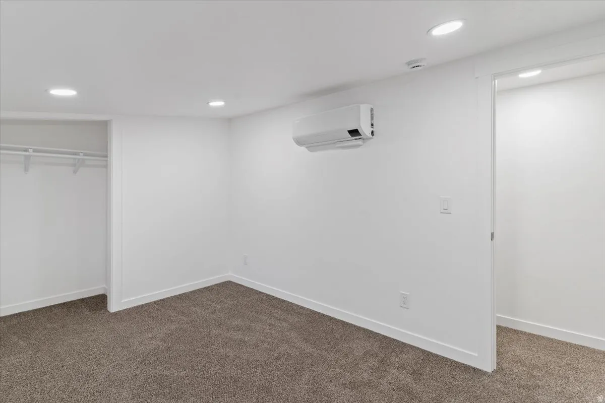 Unfurnished bedroom with dark colored carpet, a closet, a wall mounted AC, and recessed lighting
