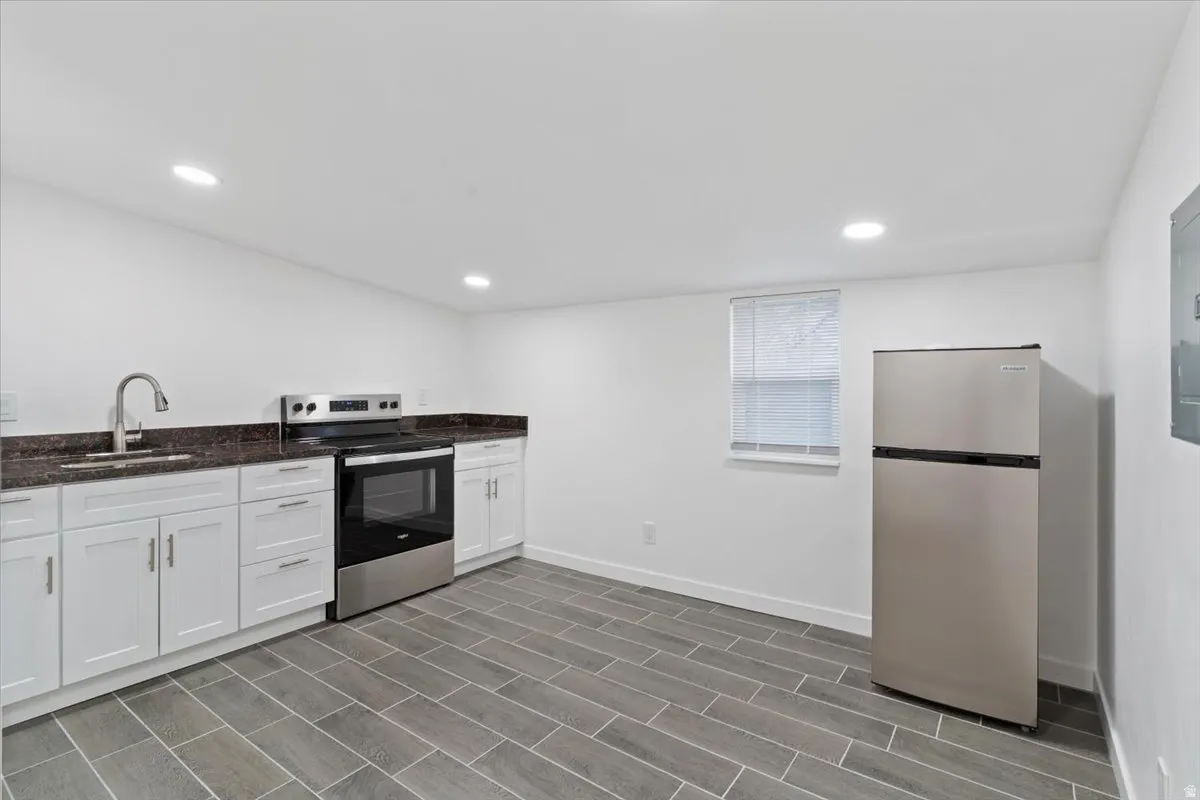 Kitchen featuring appliances with stainless steel finishes, dark stone countertops, white cabinets, recessed lighting, and electric panel