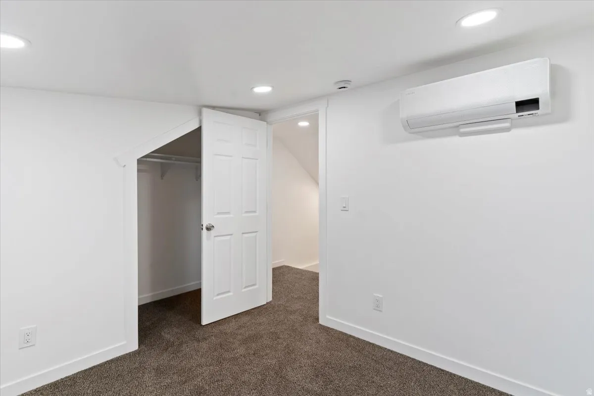 Unfurnished bedroom featuring a spacious closet, a wall mounted AC, dark carpet, and recessed lighting