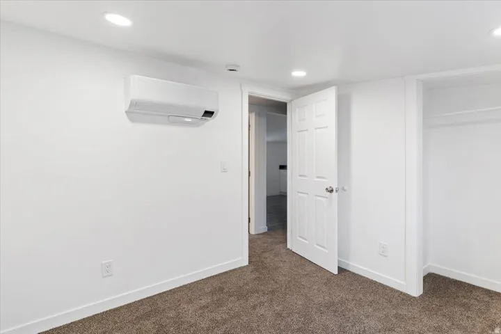Unfurnished bedroom featuring a wall unit AC and dark carpet