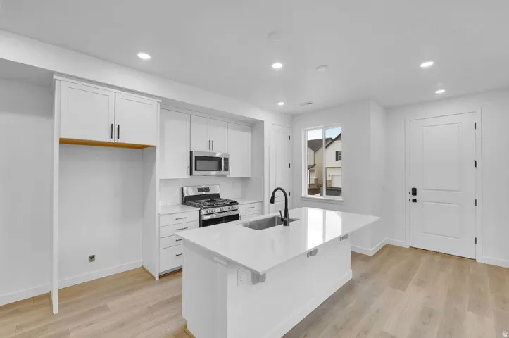 Kitchen featuring white cabinetry, stainless steel appliances, light wood finished floors, a kitchen island with sink, and recessed lighting