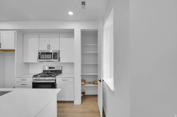Kitchen featuring stainless steel appliances, white cabinetry, light wood finished floors, decorative backsplash, and recessed lighting