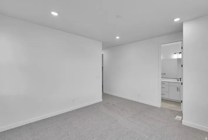 Unfurnished bedroom with light colored carpet, recessed lighting, and connected bathroom