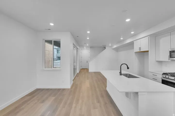 Kitchen with white cabinetry, a kitchen island with sink, recessed lighting, light wood-style floors, and light stone countertops