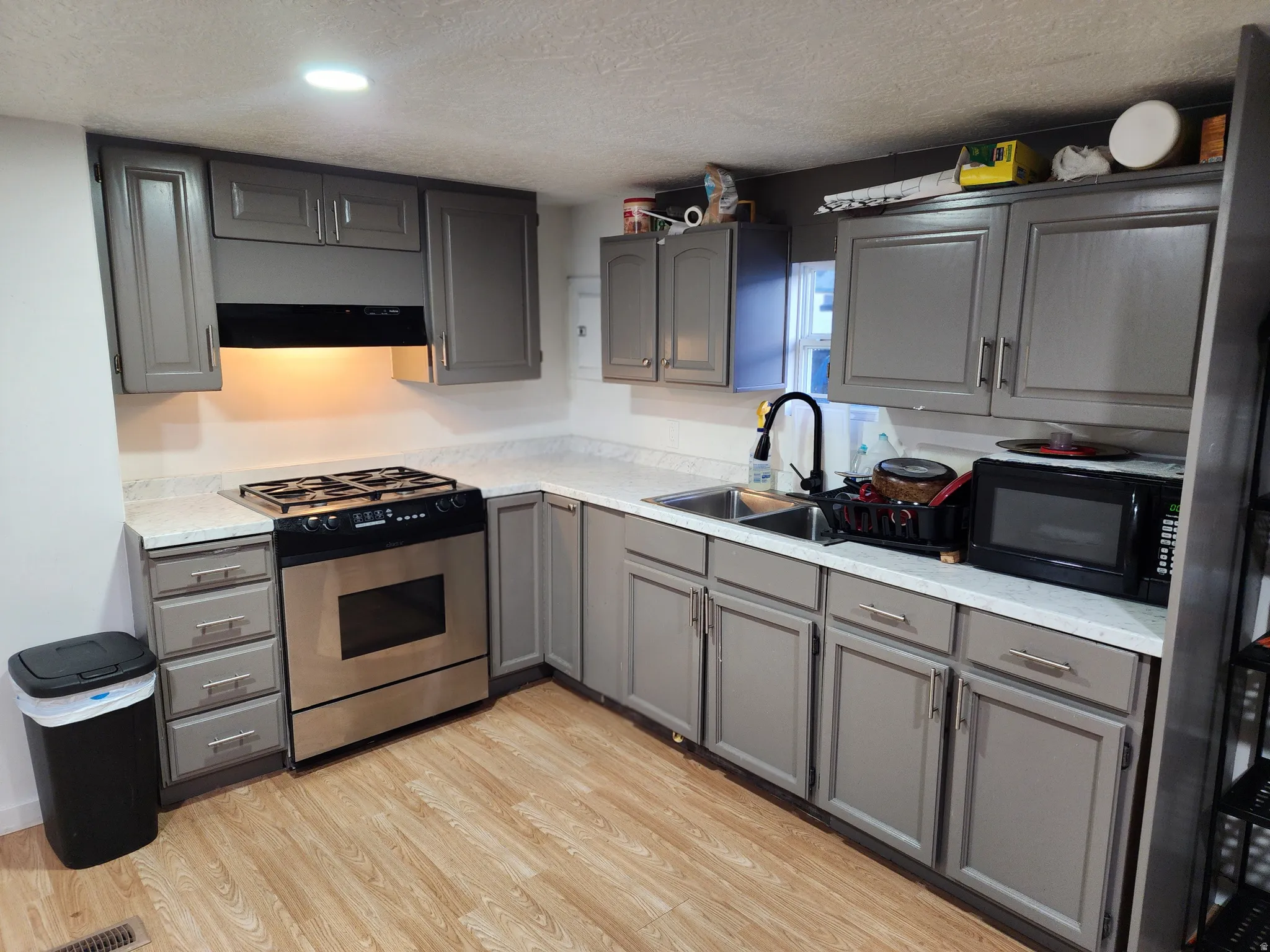 Kitchen with gray cabinetry, stainless steel appliances, light wood-type flooring, a textured ceiling, and recessed lighting