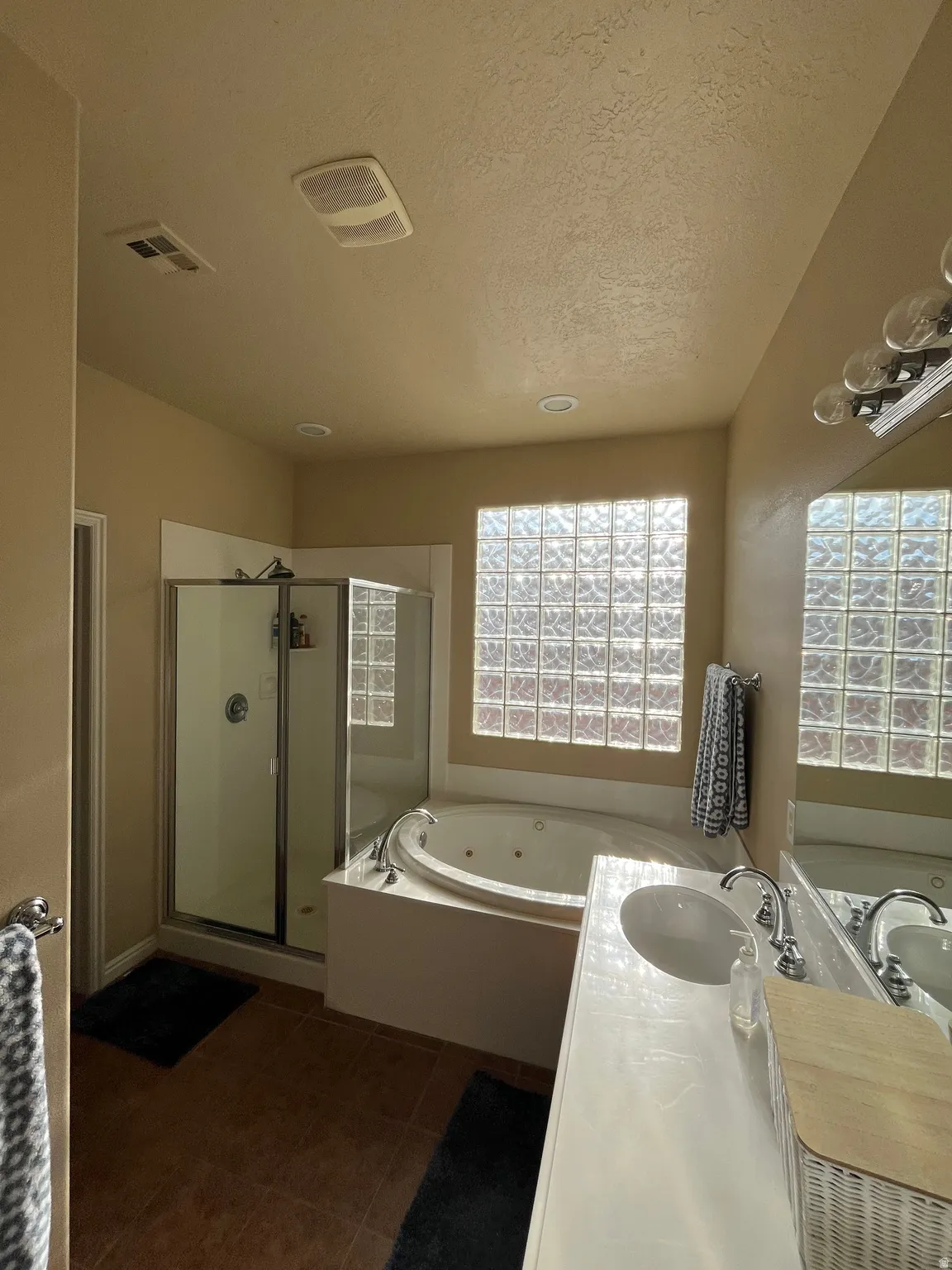 Full bathroom featuring vanity, a whirlpool tub, a stall shower, a textured ceiling, and dark tile patterned flooring