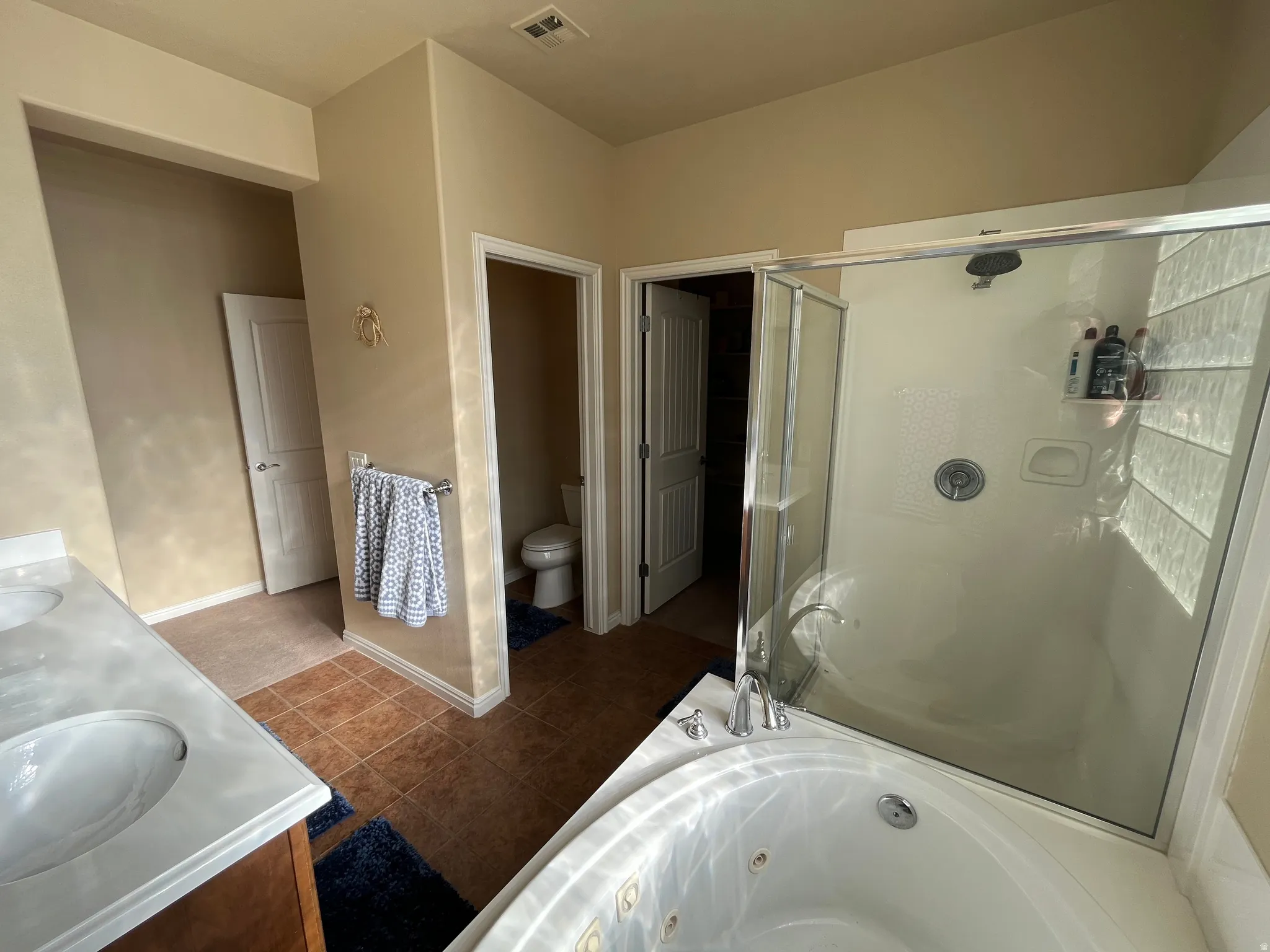 Full bath featuring a tub with jets, double vanity, a stall shower, and dark tile patterned flooring