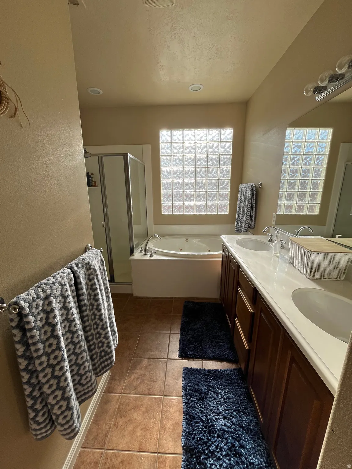 Bathroom with double vanity, a whirlpool tub, a shower stall, light tile patterned floors, and a textured ceiling