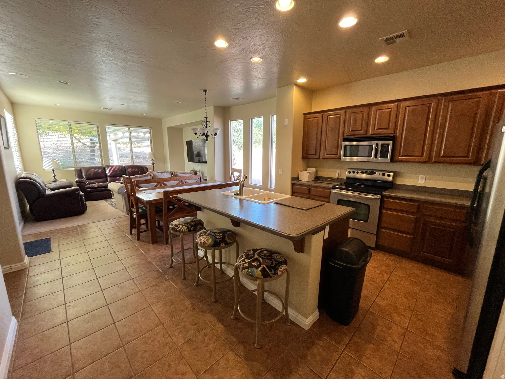 Kitchen with a textured ceiling, dark countertops, stainless steel appliances, open floor plan, and a chandelier