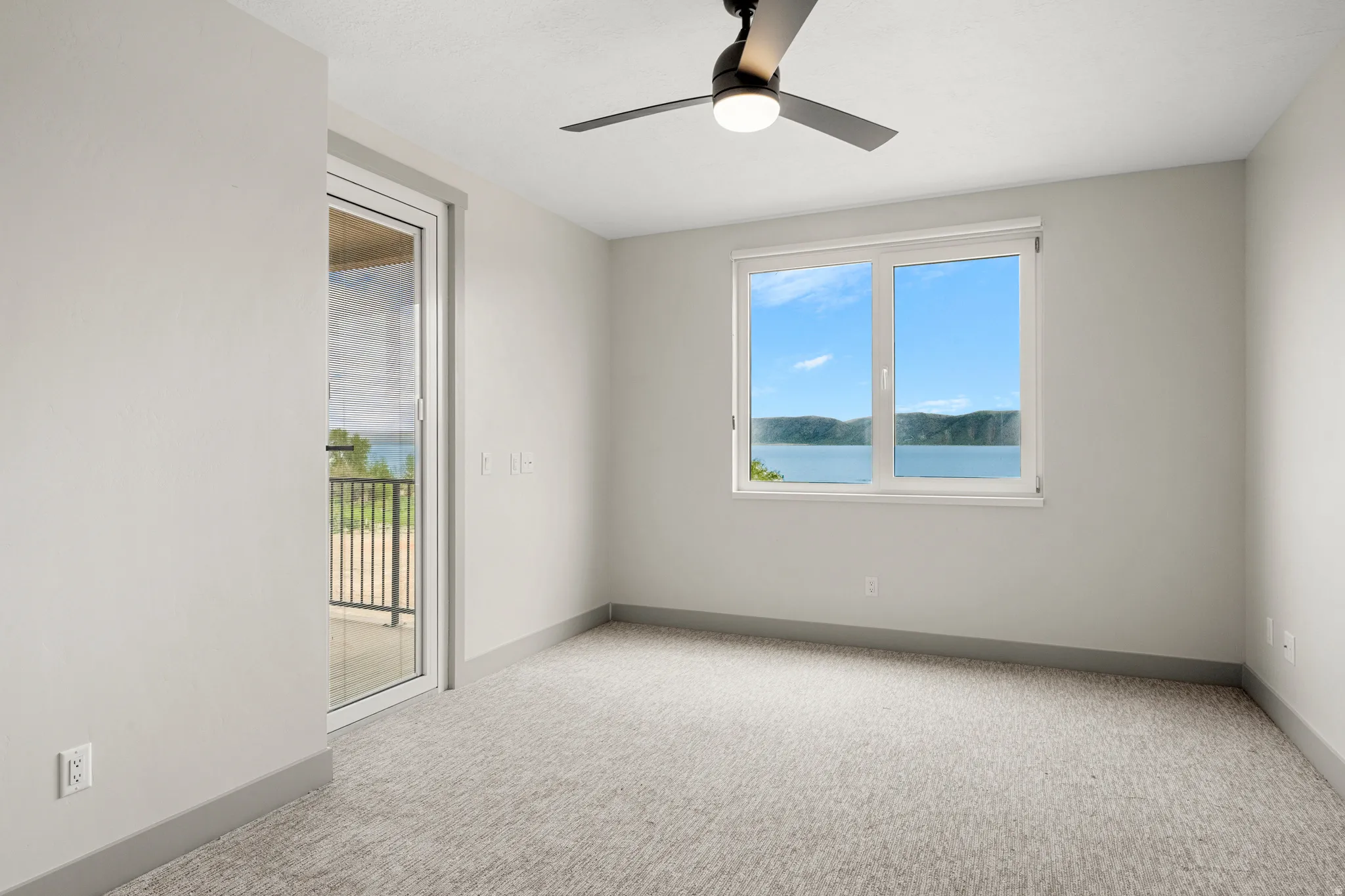 Spare room with healthy amount of natural light, light colored carpet, ceiling fan, and a water view