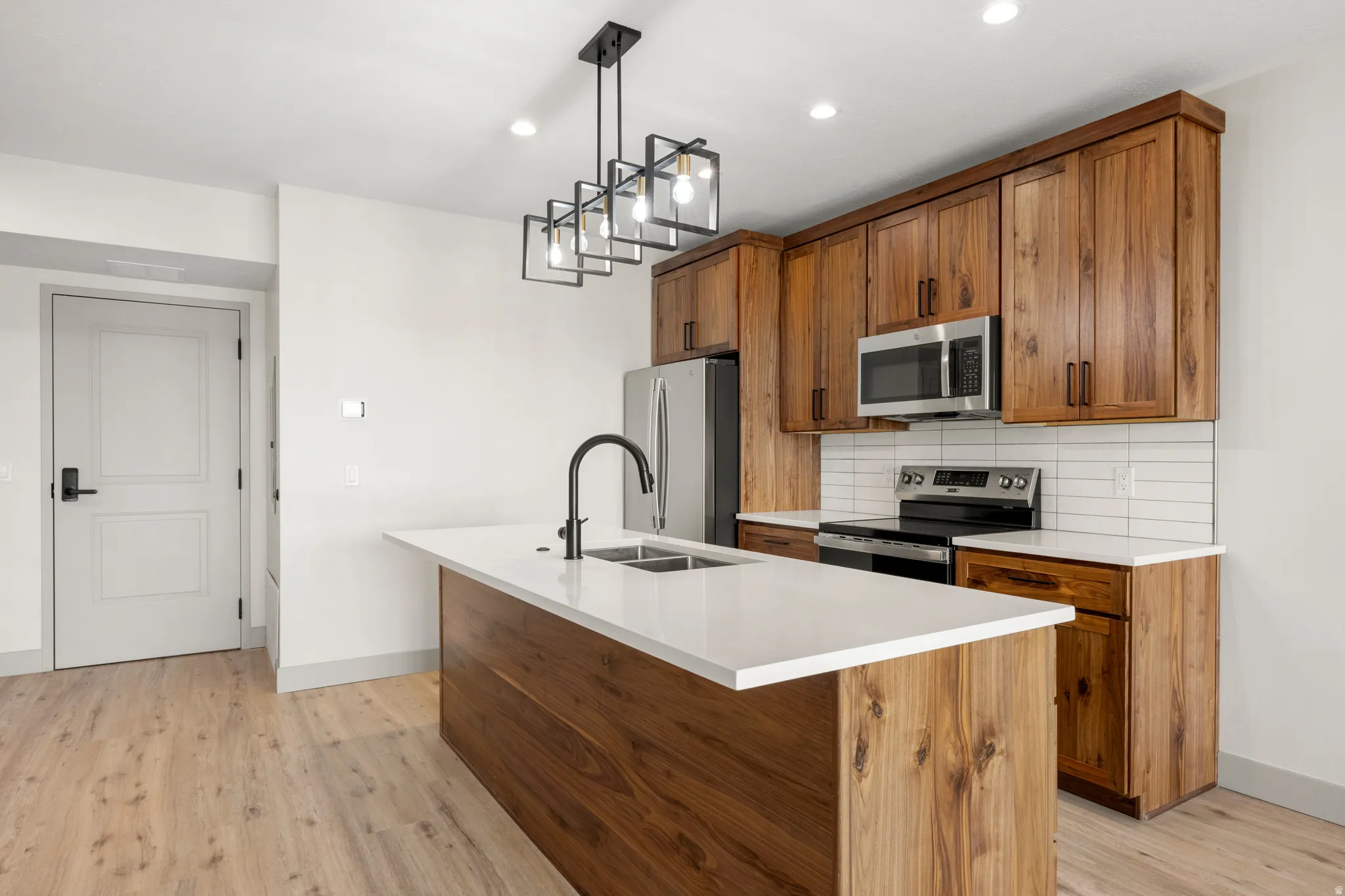 Kitchen with brown cabinetry, stainless steel appliances, tasteful backsplash, a center island with sink, and pendant lighting