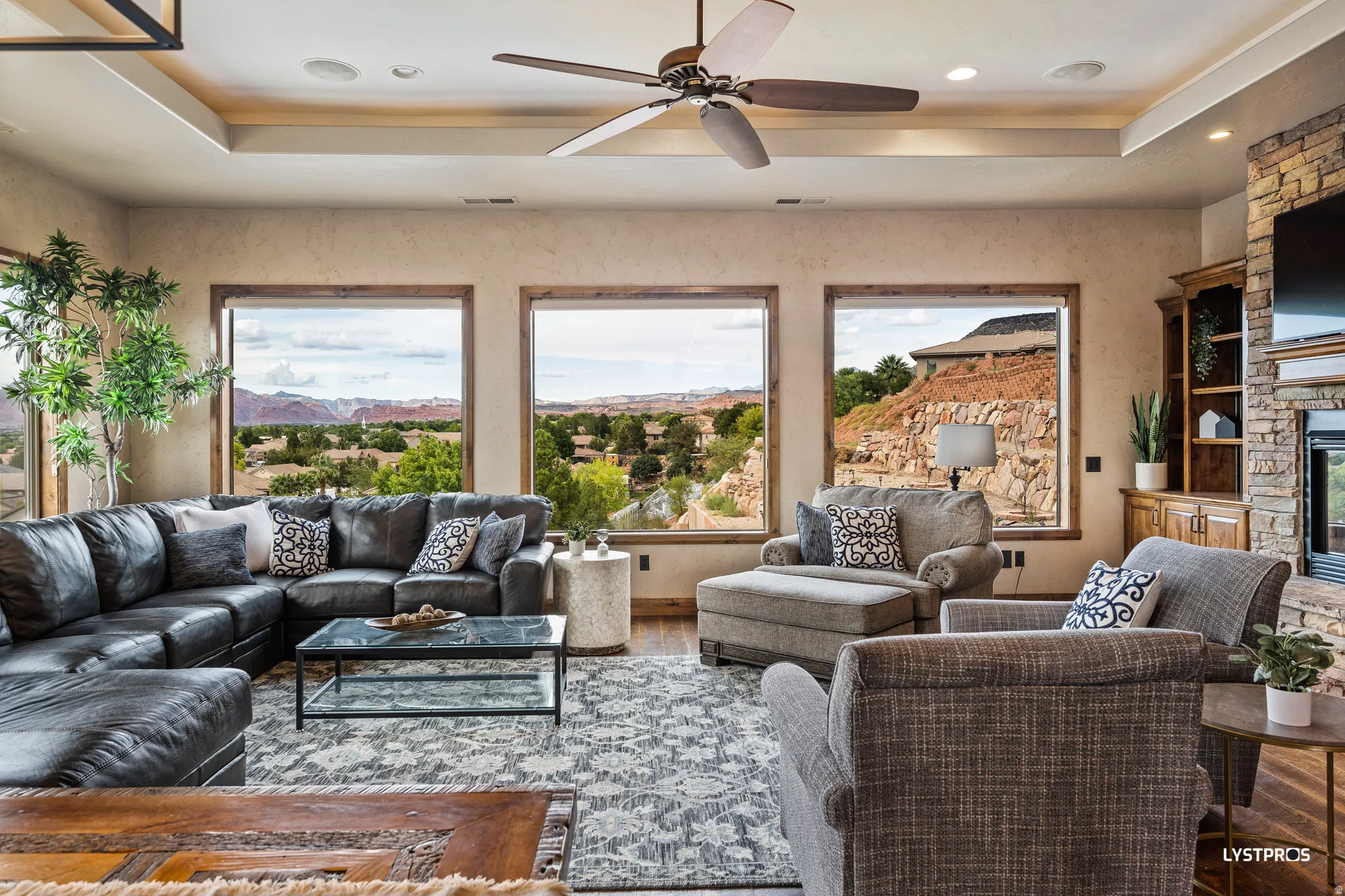 Living room with a raised ceiling, a fireplace, a ceiling fan, wood finished floors, and recessed lighting