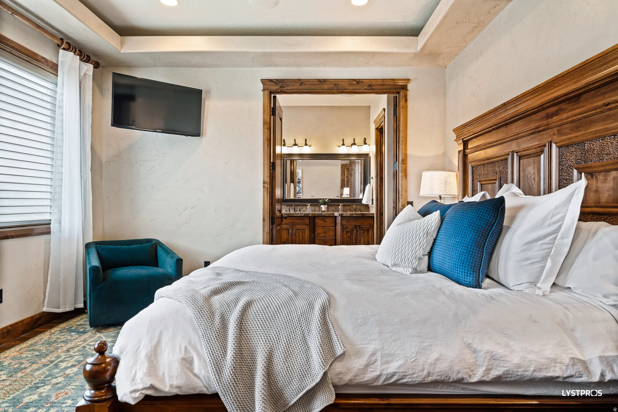 Bedroom featuring ensuite bathroom, a textured wall, recessed lighting, a raised ceiling, and wood finished floors