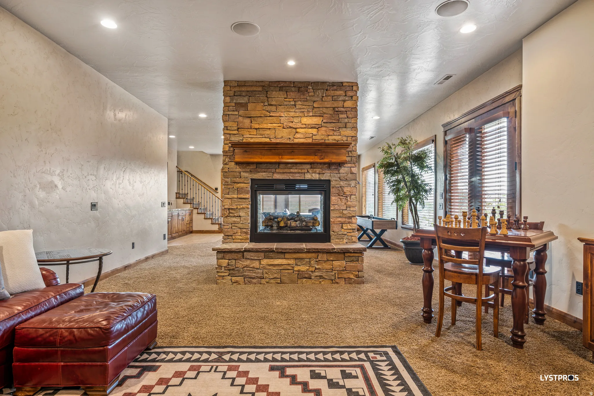 Carpeted living room with a stone fireplace, a textured wall, recessed lighting, and stairs
