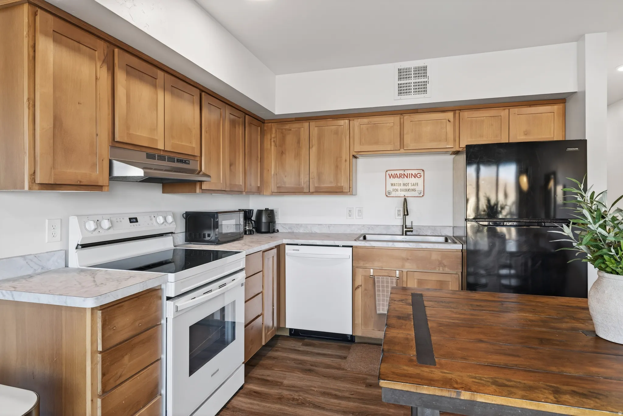 Kitchen featuring black appliances, light countertops, dark wood-style flooring, under cabinet range hood, and brown cabinets