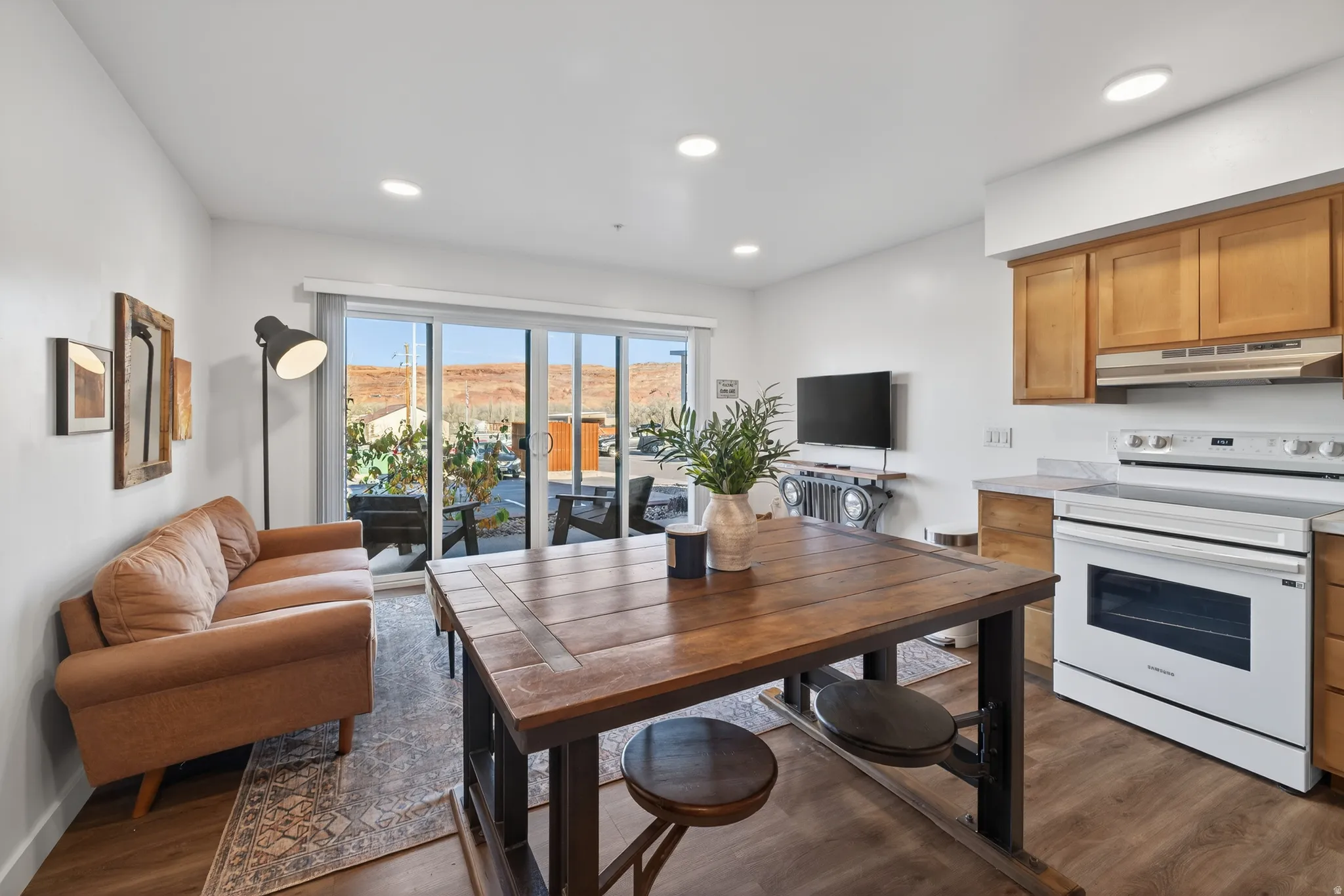 Kitchen with white range with electric stovetop, brown cabinets, light countertops, dark wood-style floors, and under cabinet range hood