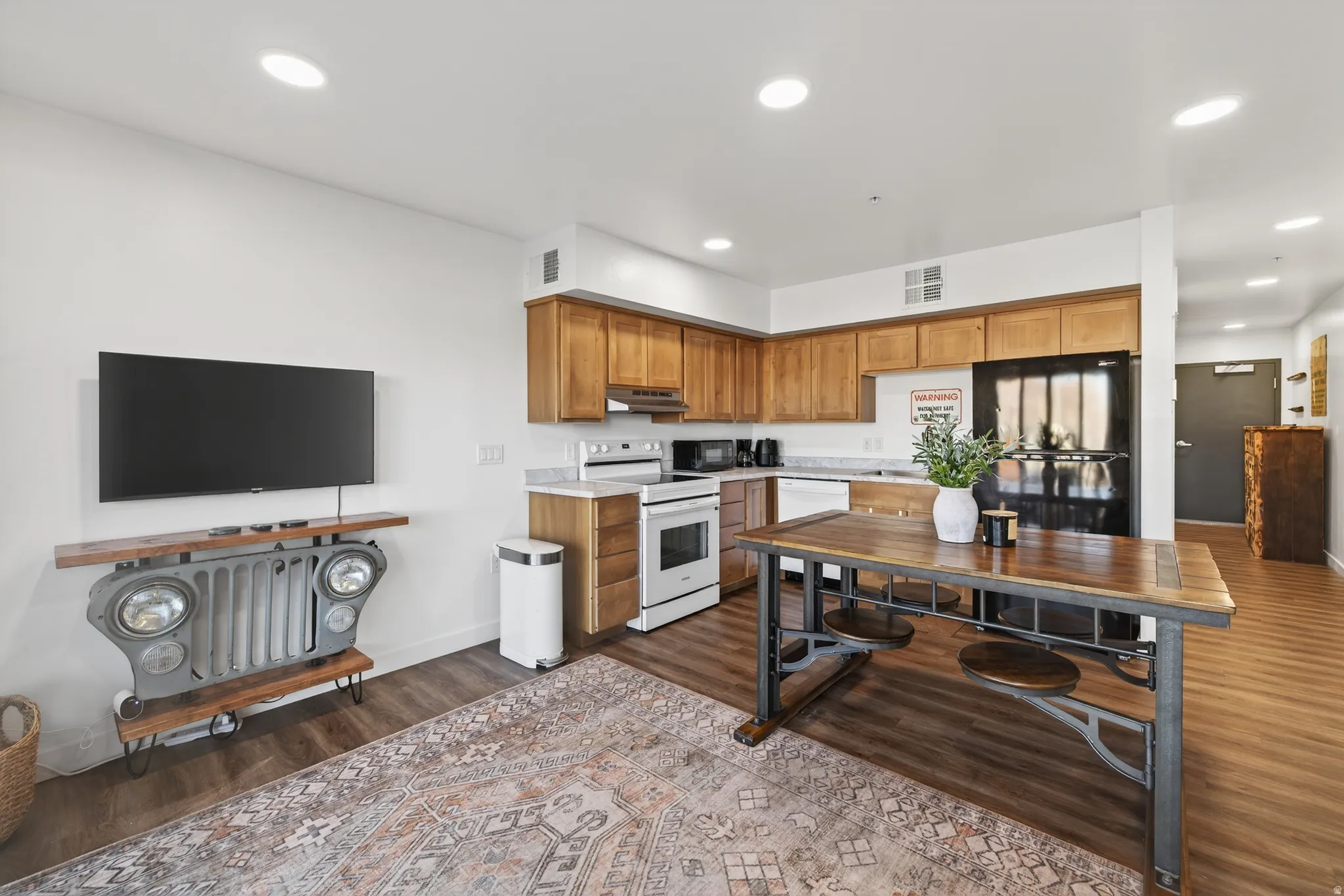 Kitchen featuring brown cabinets, light countertops, black appliances, dark wood finished floors, and recessed lighting