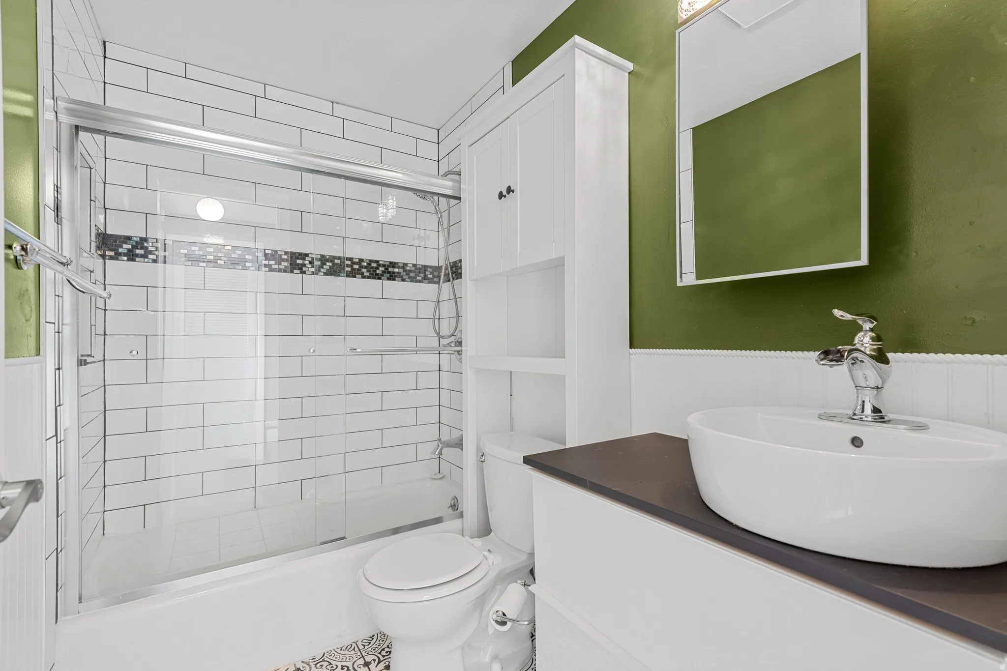 Full bath with bath / shower combo with glass door, vanity, and wainscoting