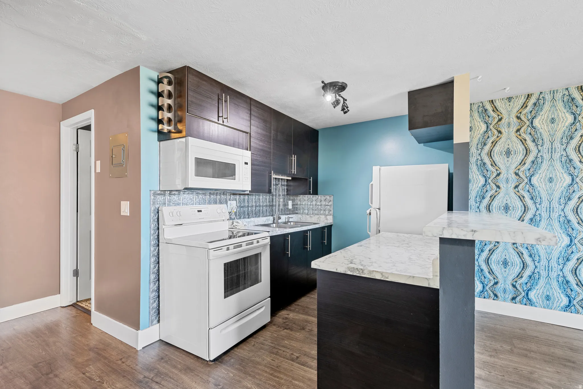Kitchen featuring white appliances, light countertops, a breakfast bar, tasteful backsplash, and dark wood-style flooring
