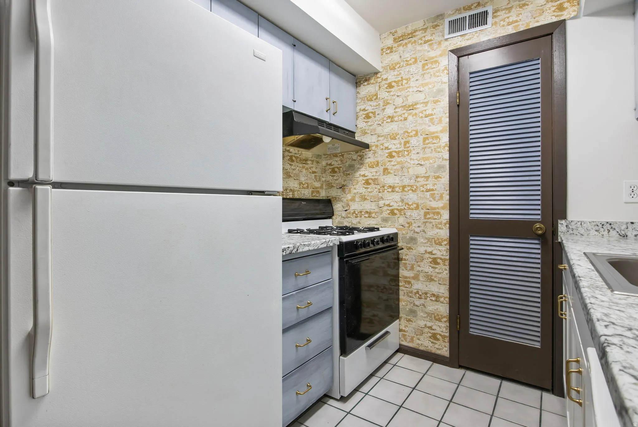 Kitchen featuring freestanding refrigerator, gas stove, light tile patterned floors, under cabinet range hood, and gray cabinetry