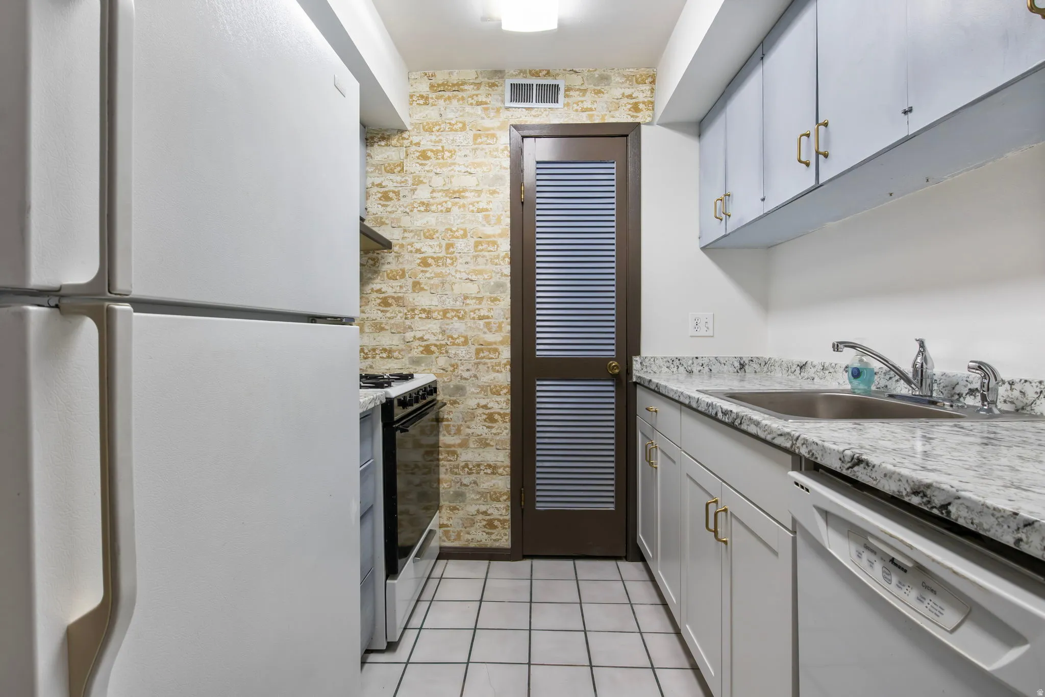 Kitchen with white appliances, light stone countertops, and light tile patterned floors