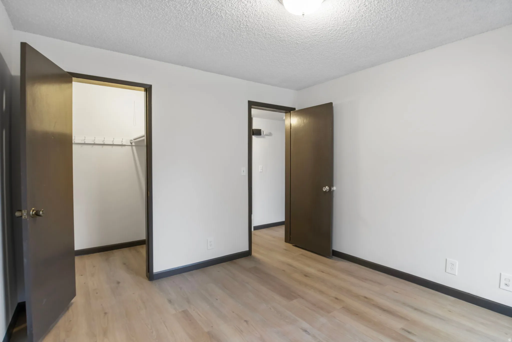Unfurnished bedroom with a spacious closet, a textured ceiling, and light wood-style floors