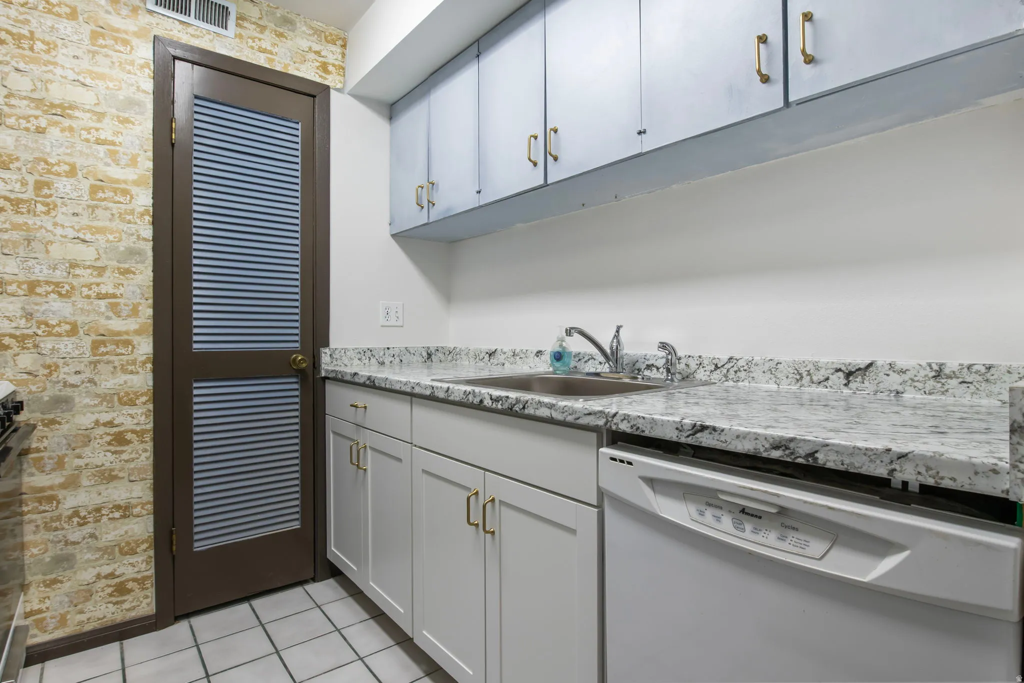 Kitchen with dishwasher, brick wall, light tile patterned floors, and stainless steel range oven