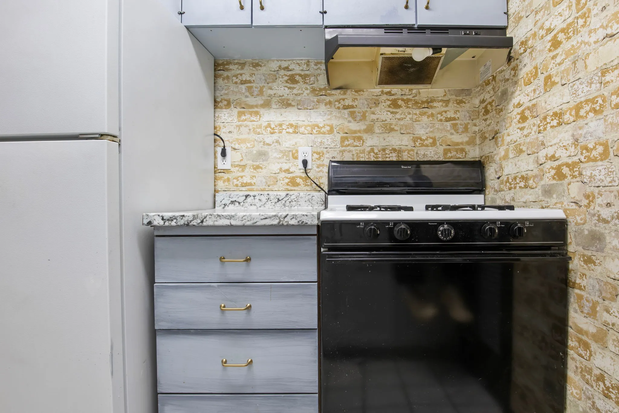 Kitchen featuring range with gas cooktop, freestanding refrigerator, under cabinet range hood, and gray cabinets