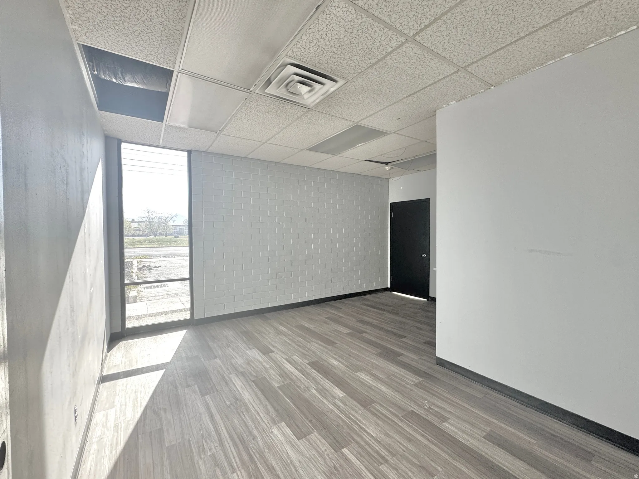 Unfurnished room featuring light wood finished floors, a drop ceiling, and expansive windows