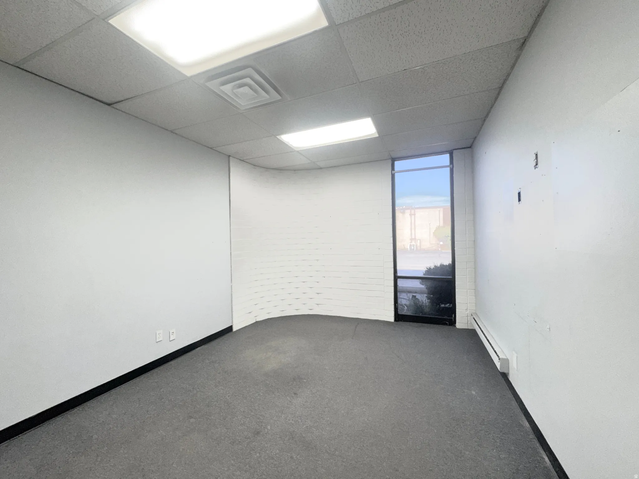 Empty room with dark carpet, a baseboard radiator, a paneled ceiling, and expansive windows